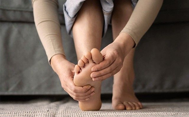 Eine Person sitzt auf dem Boden und umgreift oder massiert mit beiden Händen den eigenen nackten Fuß.